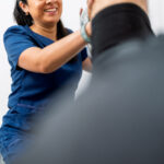 Female physiotherapist smiling, supporting a male patient's leg for rehabilitation exercise during a physical therapy session
